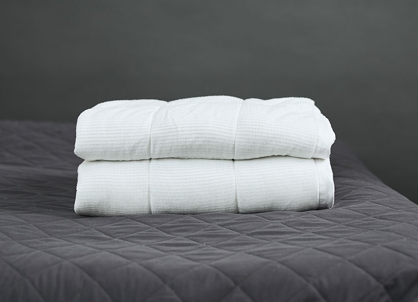 A weighted duvet folded on top of a bed with a dark grey bed spread