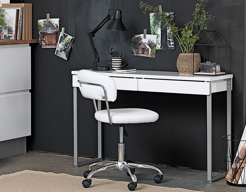 Klein wit bureau met lades en een witte bureaustoel tegen een donkere muur 