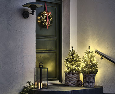 Verlichte kunstkerstboom met lichtsnoer en krans aan de deur