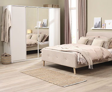 Slaapkamer met witte kledingkast met spiegeldeuren en beige tweepersoonsbed