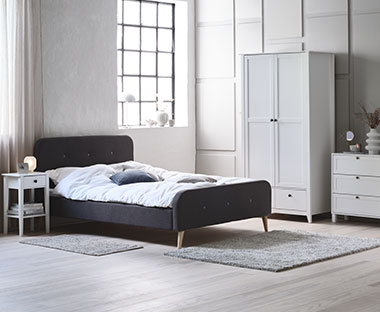 Donkergrijs bedframe van stof en massief hout in een slaapkamer met witte kasten