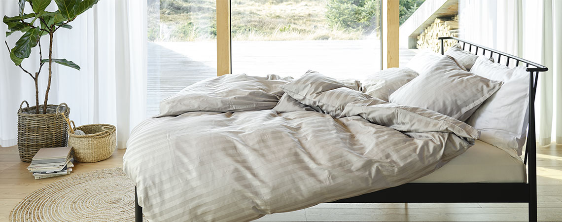 Slaapkamer met zwart metalen bed, dekbedden en kussens, overtrokken met gestreept beddengoed in lichtgrijs en wit 