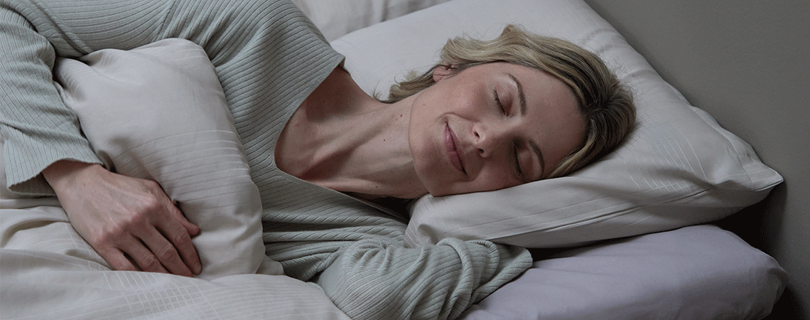 Vrouw slaapt op haar zij in bed met wit kussen en dekbed