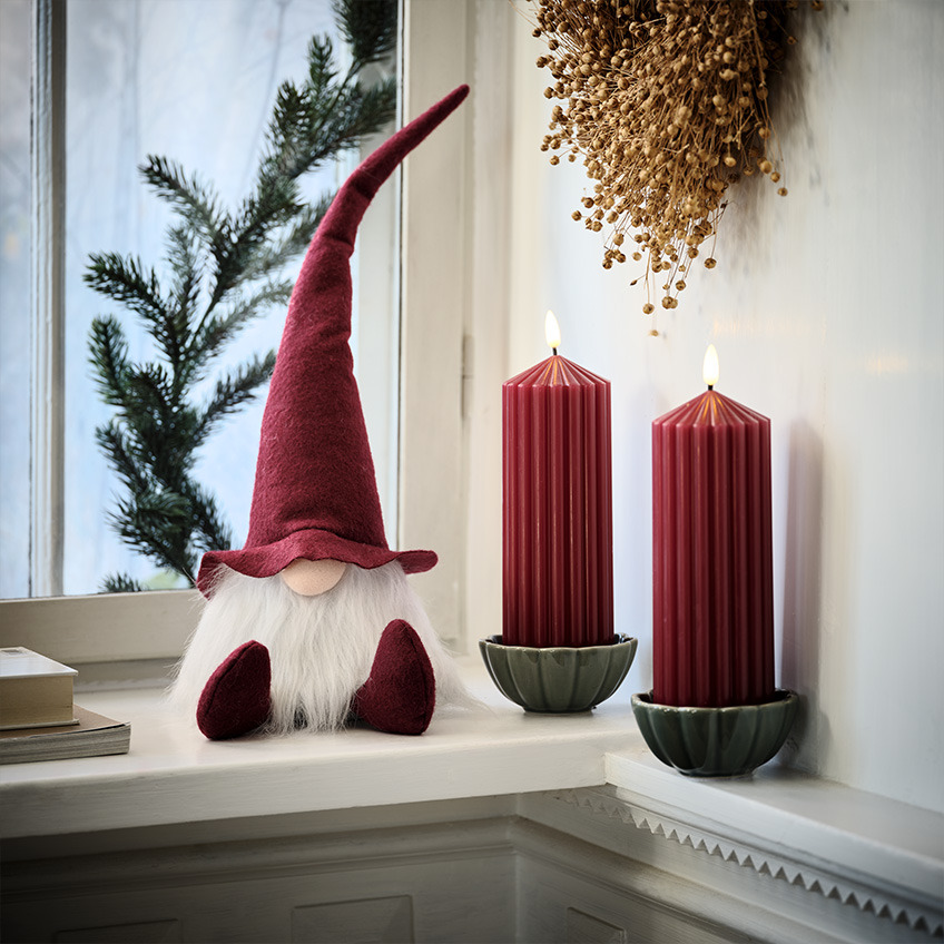 Scandinavische kerstman op vensterbank naast grote, rode kaarsen  