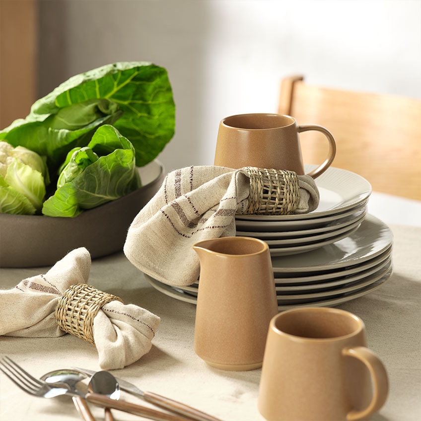 Servies: Witte dinerborden en witte dessertborden, mok, melkkan, stoffen servetten met servetringen en slakom op eettafel