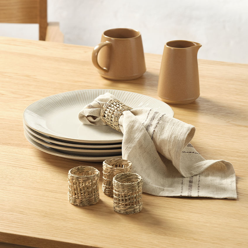 Witte gecanneleerde dinerborden, melkkannen, stoffen servet en servetringen op eettafel