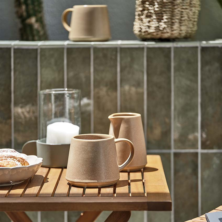 Koffiemok en melkkannetje op houten tuintafeltje in de volle zon 