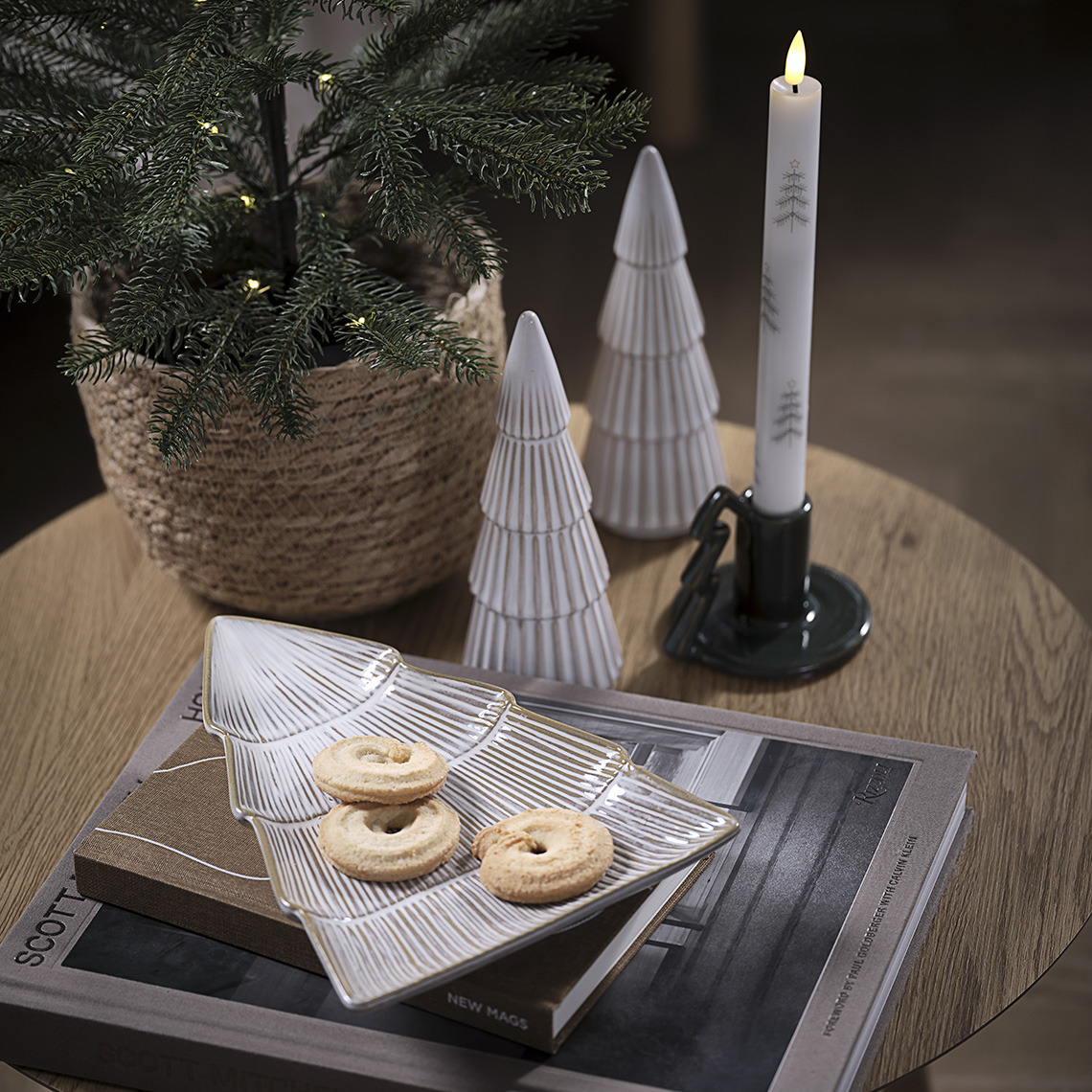 Schaal met koekjes, twee decoratiebomen en kandelaar met kaars op een tafel 