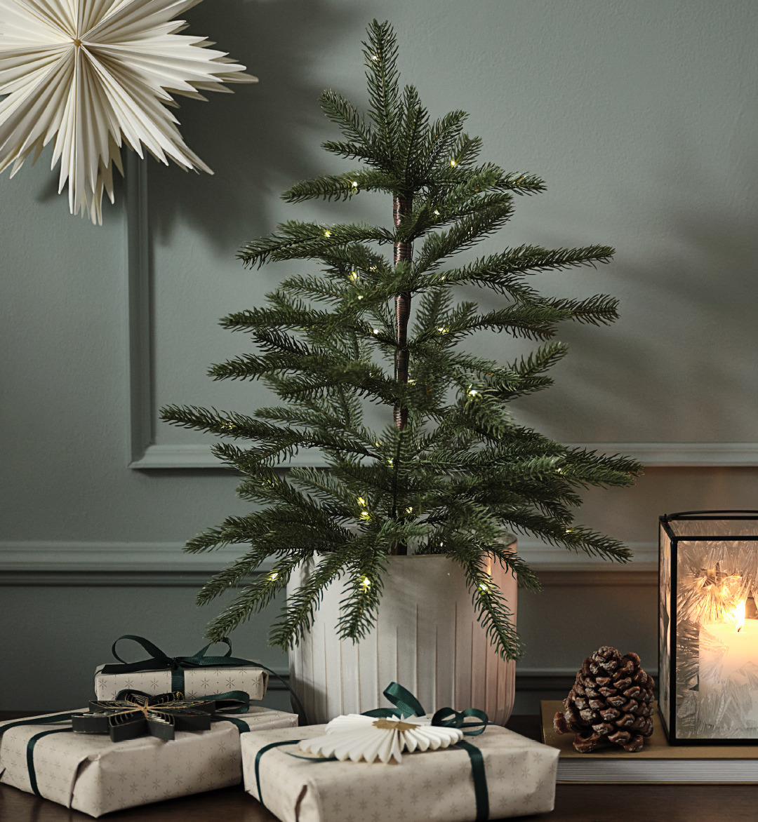 Kunstkerstboom in een pot met lichtjes en een papieren ster aan de muur 