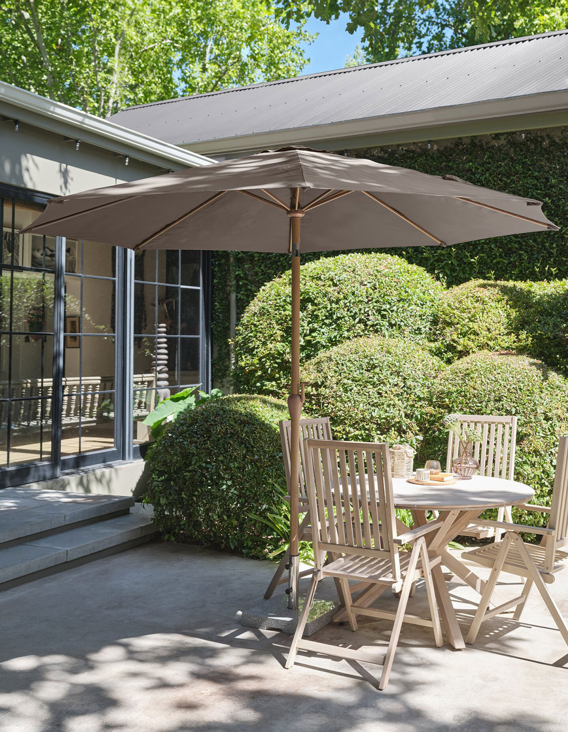 Grote beige parasol op een terras met een tuintafel en tuinstoelen