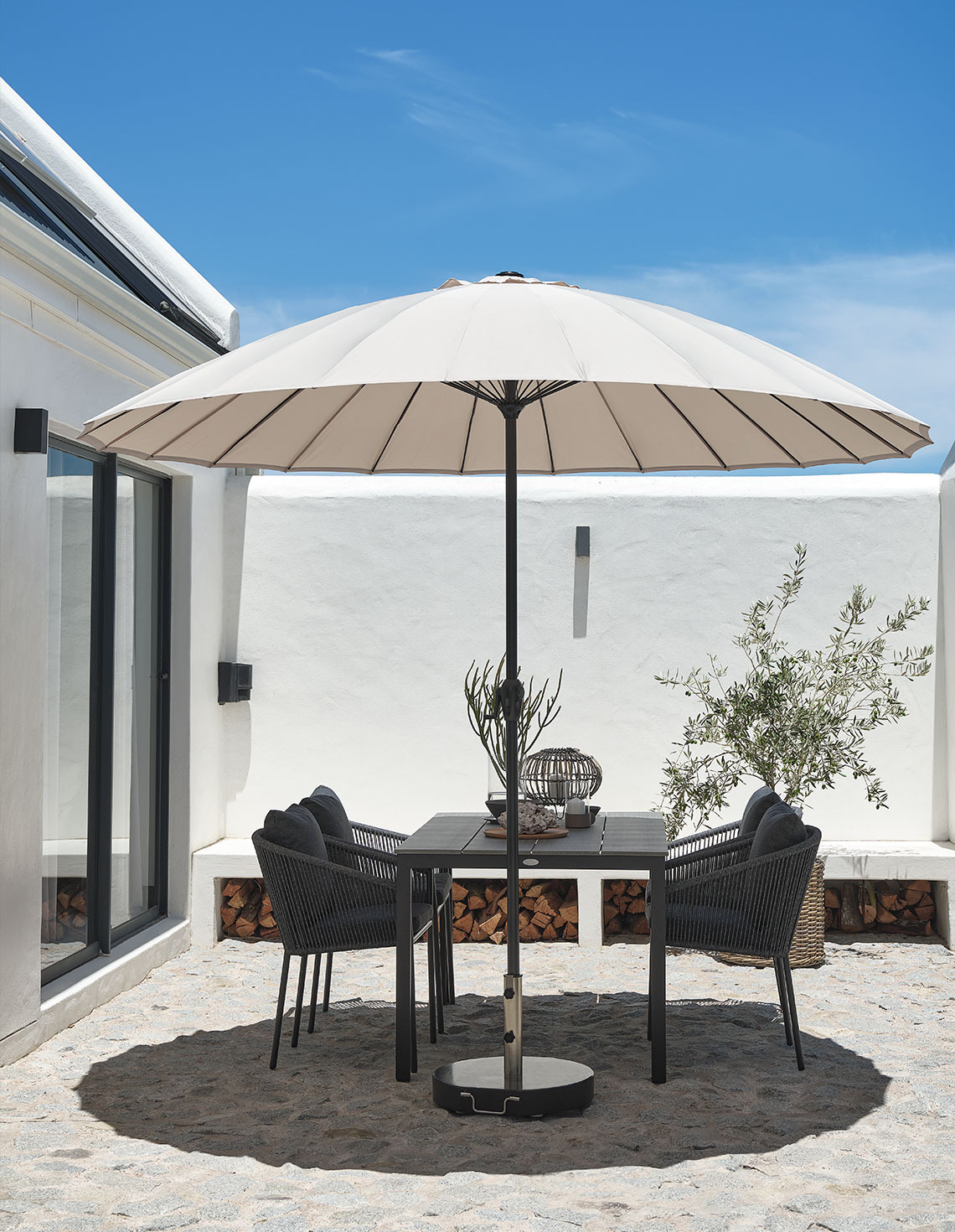 Klassieke beige parasol op een terras met een tuintafel en tuinstoelen