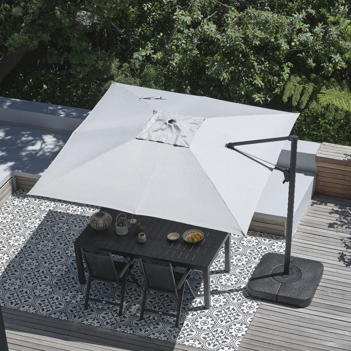 Grote, vierkante grijze hangende parasol boven een eettafel buiten met tuinstoelen