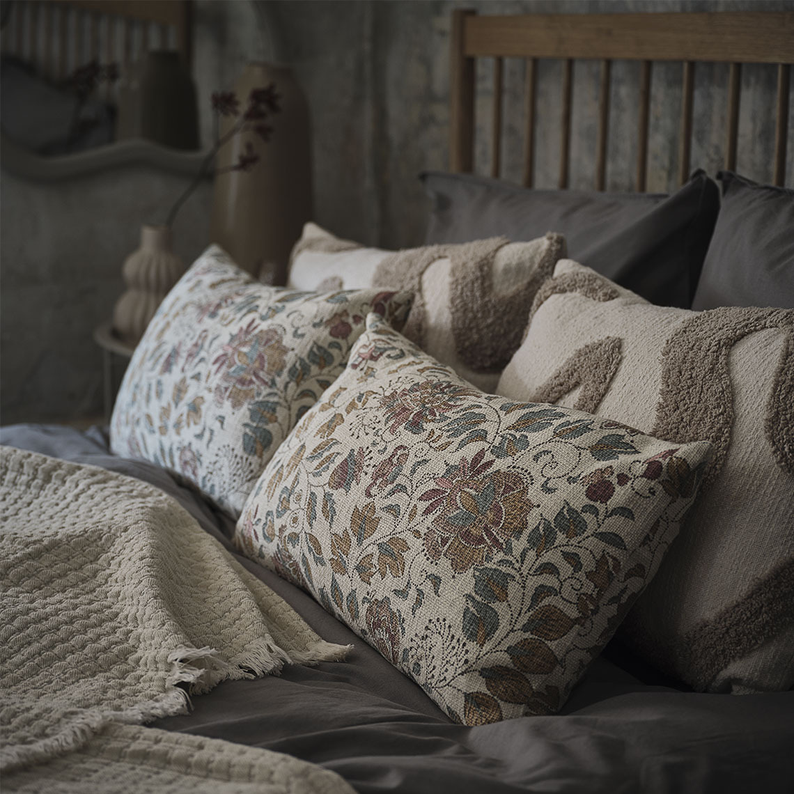 Sierkussens met bloemenprint en beige kussens op bed met een beige plaid