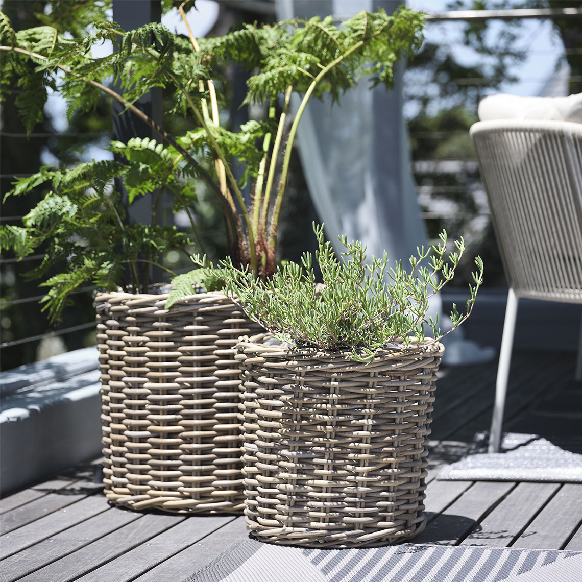 SEGLA plantenbakken Twee plantenbakken in naturel rotan op een balkon