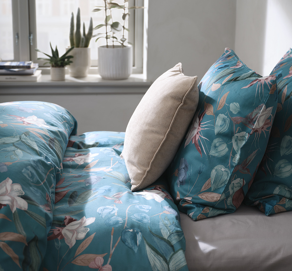 Een slaapkamer met een bloemen dekbedovertrek en een extra kussen in de contrasterende kleur
