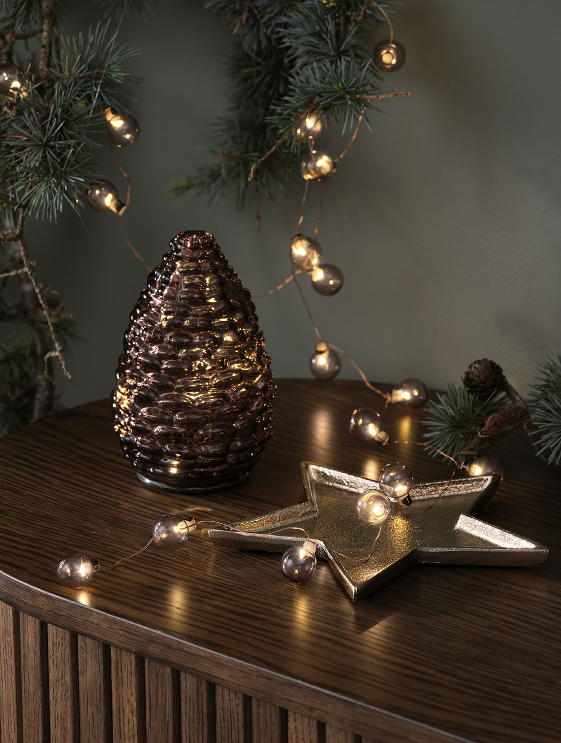 DELLING kerstkrans en ALV lichtsnoer Decoratieve kerstverlichting zoals een glazen dennenappel en een lichtsnoer met gouden kerstballen op een dressoir