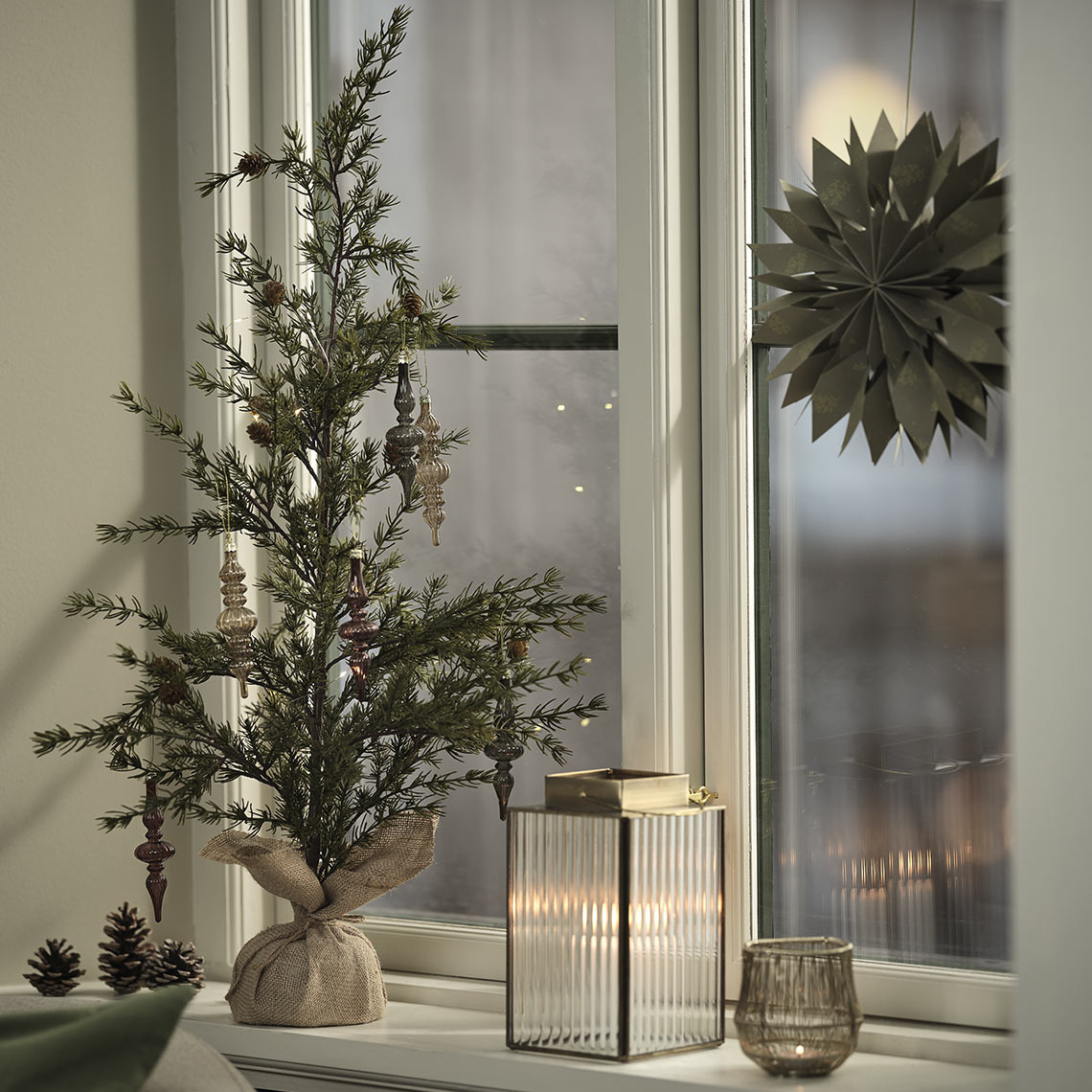 Tealight holder, lantern and artificial Christmas tree with decorations in windowsill 
