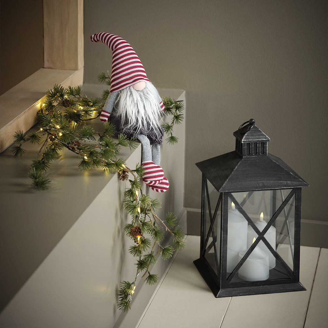 SVADILFARI kerstelf en PULKA lantaarn Kerstelf met muts, handschoenen en sokken met rode strepen naast een zwarte lantaarn