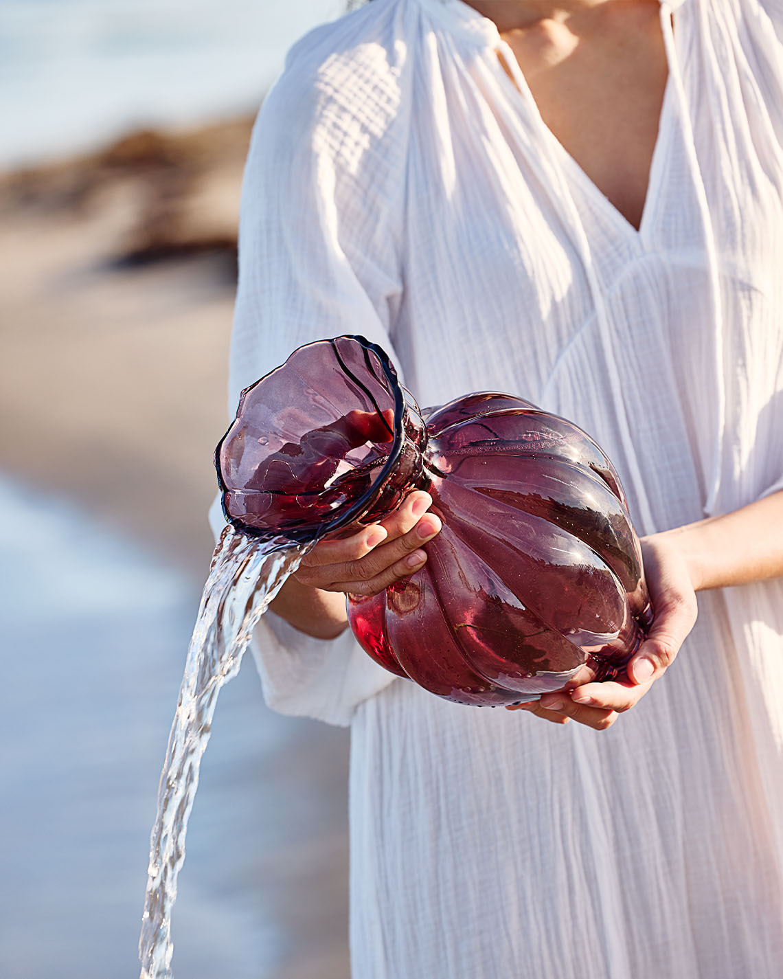 VILMER vaas Glazen vaas in auberginekleur, vastgehouden door een vrouw op het strand