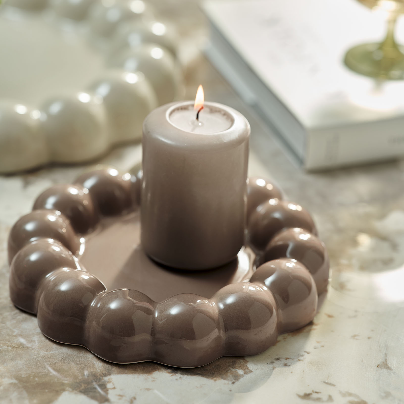 Een brandende kaars en een licht chocoladebruin decoratief dienblad met bobbelige randen