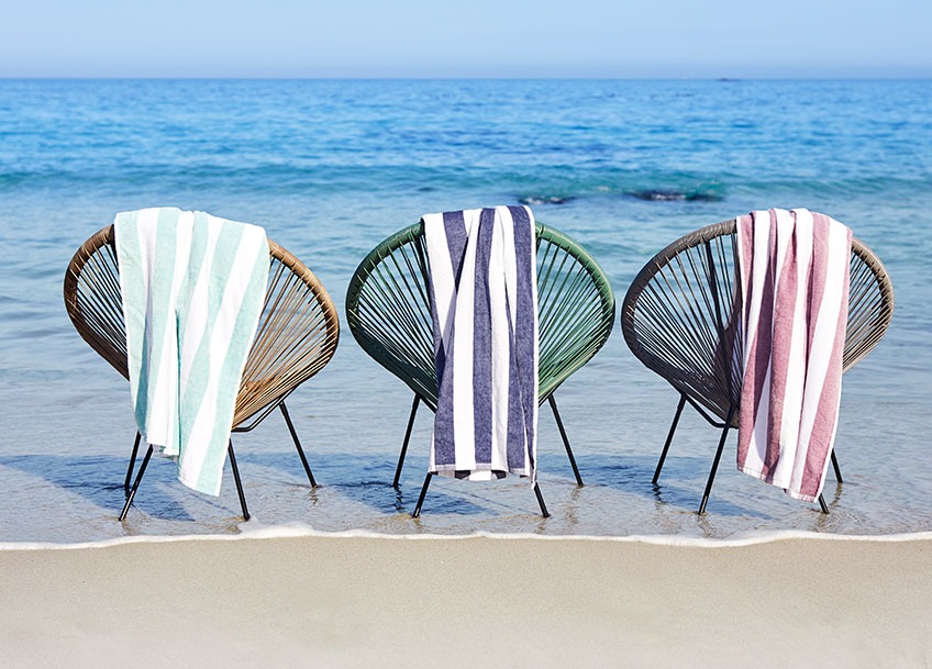 Garden lounge chairs on a beach with large beach towels hanging from the back 