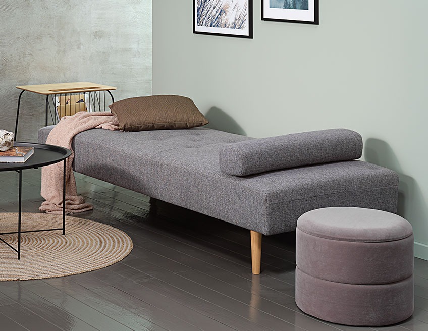 Storage pouffe beside a grey daybed with a cushion and a throw