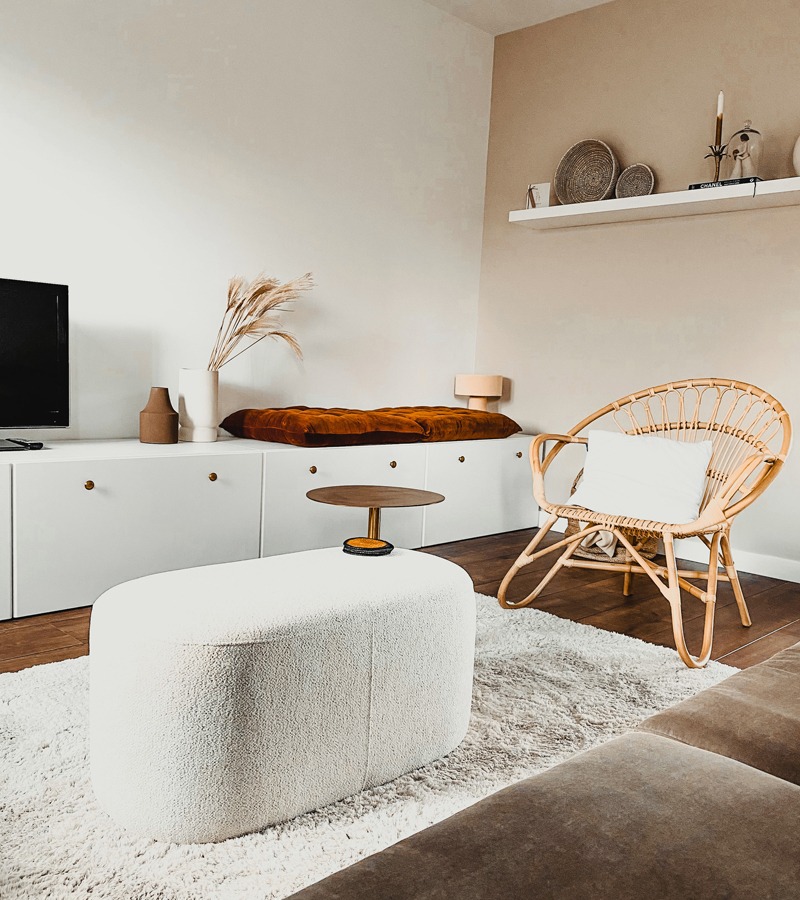 Witte poef in een woonkamer met vloerkleed, bank en rotan fauteuil