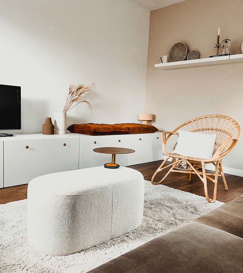 Poef OREBO en fauteuil BELLELUND rotan Witte poef in een woonkamer met vloerkleed, bank en rotan fauteuil