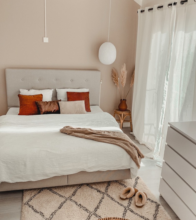 Slaapkamer met wit dekbedovertrek, sierkussens en een zacht vloerkleed