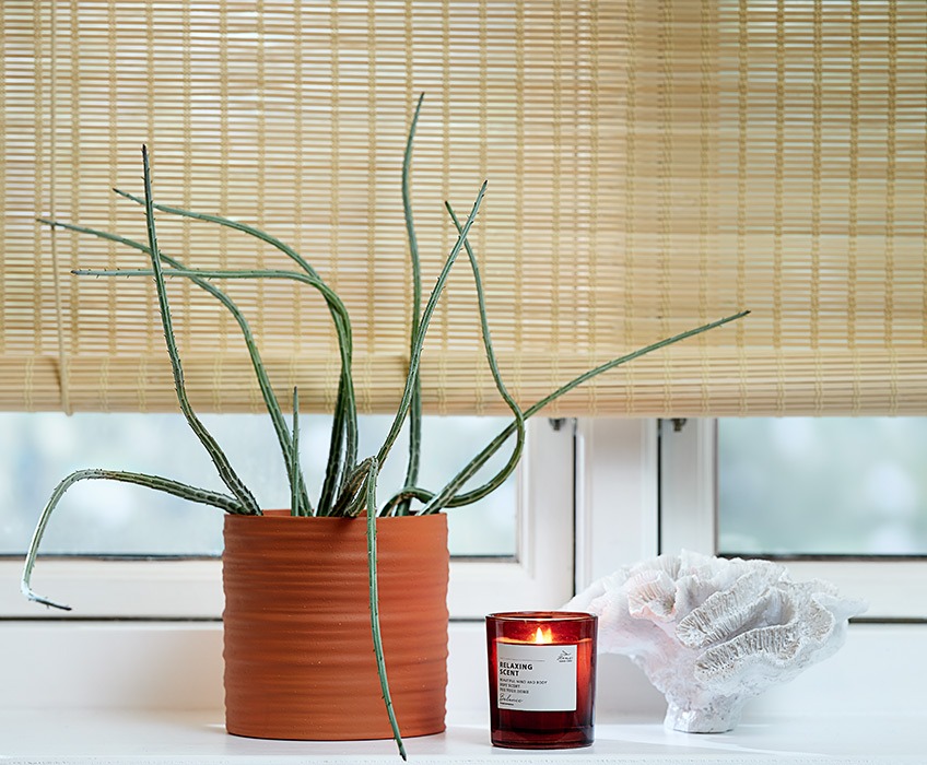 Bamboe rolgordijnen voor het raam met een plantenpot, een geurkaars en een ornament in de vensterbank