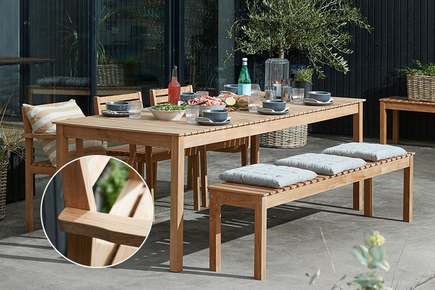 patio with a teak garden bench and chairs by a table ready for dinner 