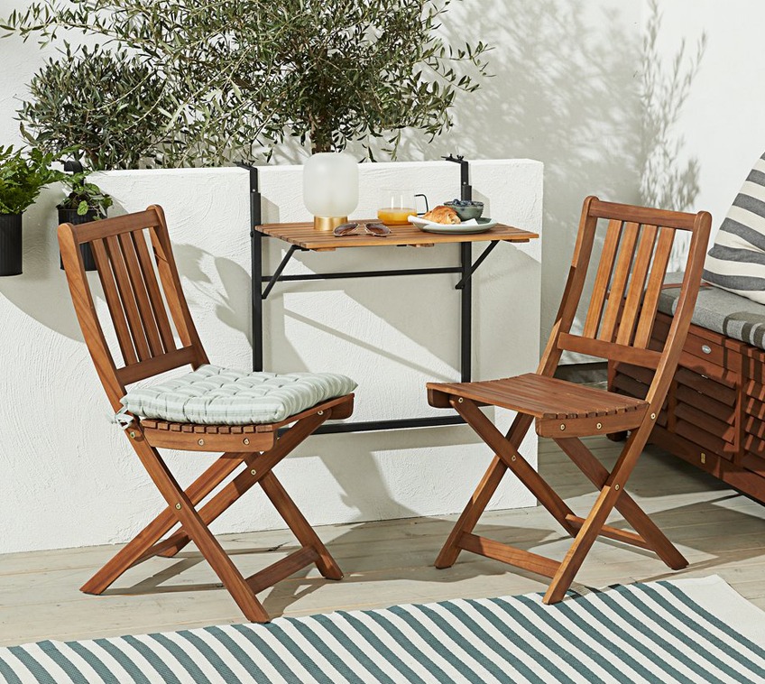 Twee houten klapstoelen en een balkontafel op een balkon met een vloerkleed