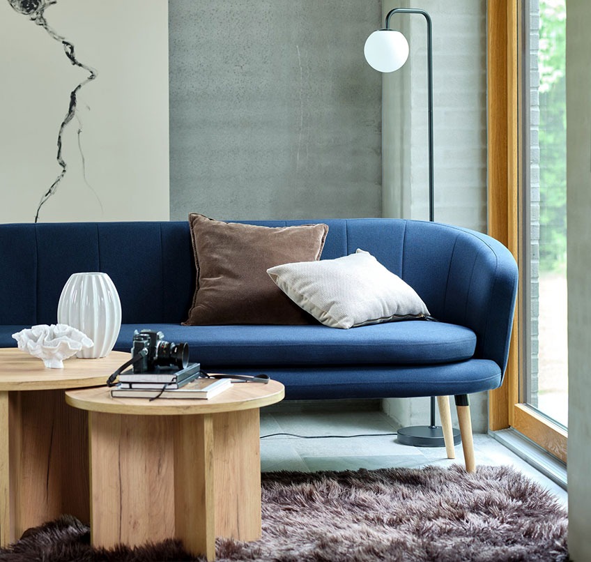 GISTRUP bank, KALVEHAVE salontafels en ADRIAN staande lamp Blauwe bank, ronde salontafels, bruin vloerkleed en een lamp