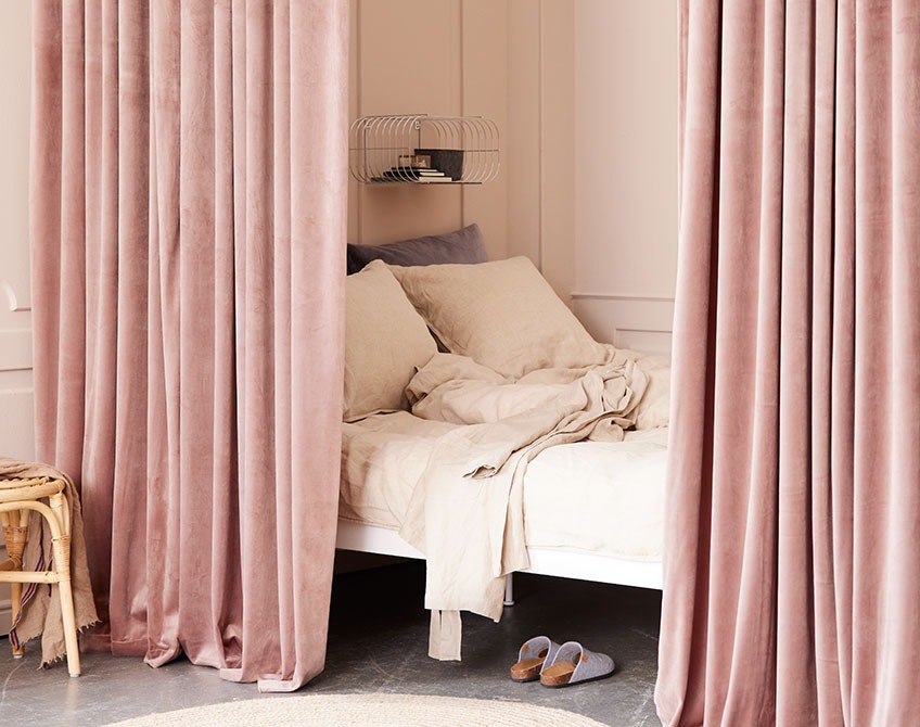 Roze gordijnen gebruikt om een slaapruimte af te scheiden van een grote woonkamer