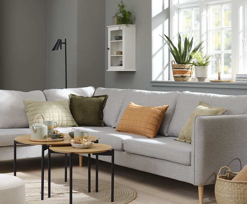 Woonkamer ingericht met een grijze sofa met daarop oranje, groene en beige kussens