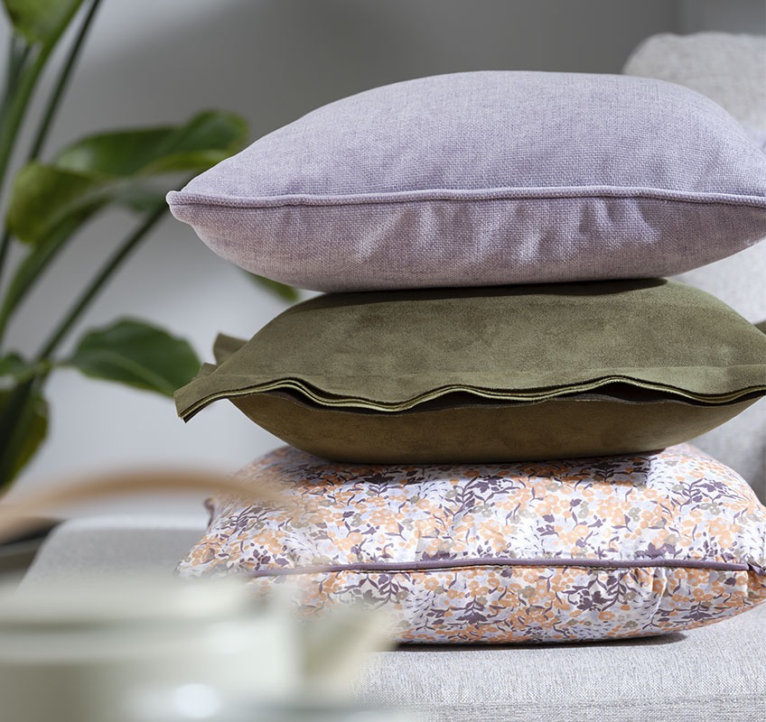 Stapel van drie kussens: een paarse, een groene en een met bloemenprint
