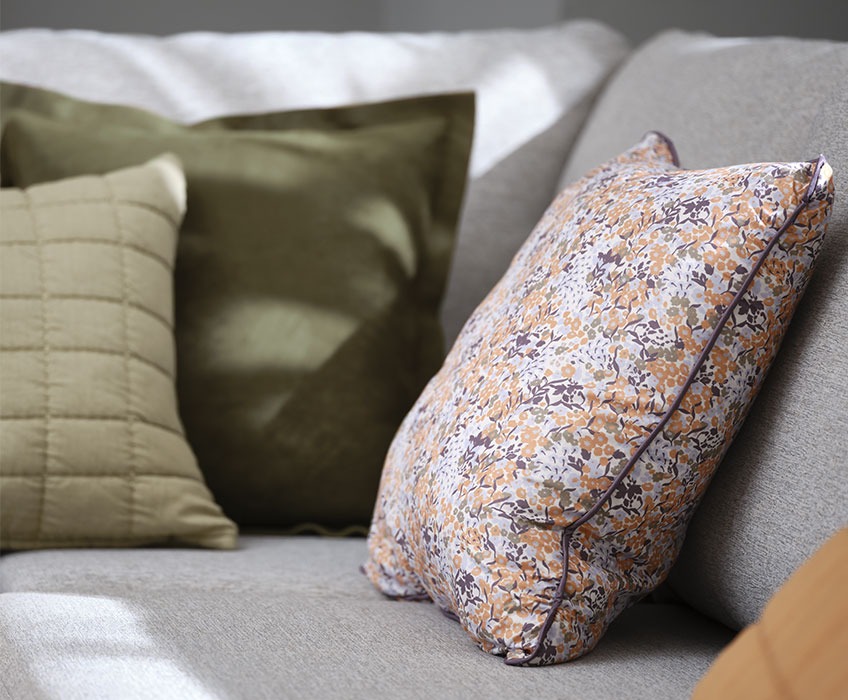 KAMILLE sierkussen met bloemenprint, ALM groene suède kussen en VALUME gewatteerde kussen Grijze bank met groene en fleurige bloemenprint kussens