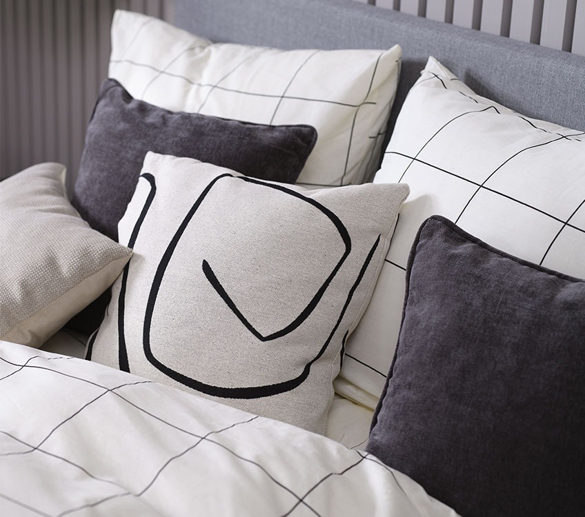 Slaapkamer met wit met zwart dekbedovertrek, zwart nachtkastje en decoratieve kussens
