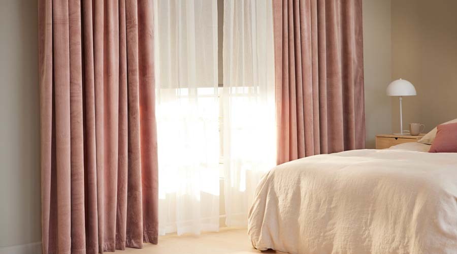 Roze overgordijn van fluwelen stof, in between gordijn en een rolgordijn in een slaapkamer