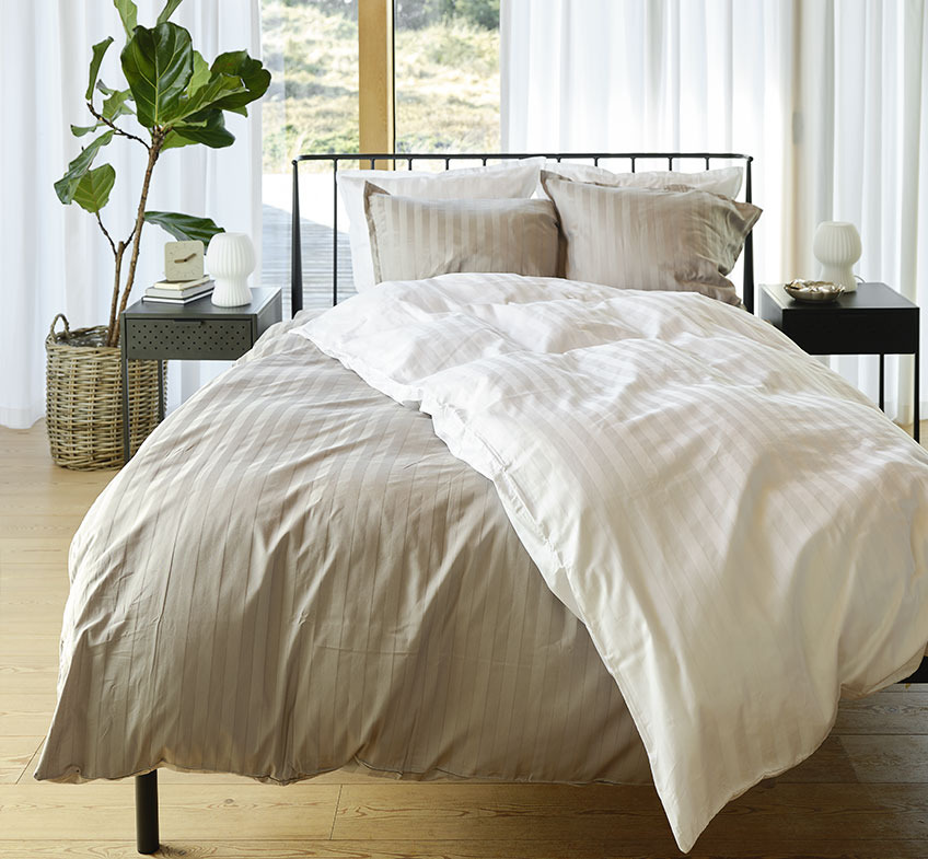 Slaapkamer met grijs en wit gestreept beddengoed op het bed en twee nachtkastjes 
