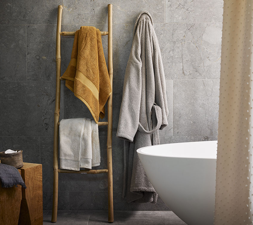 Decorative ladder with yellow and white towel and light grey bathrobe in a bathroom