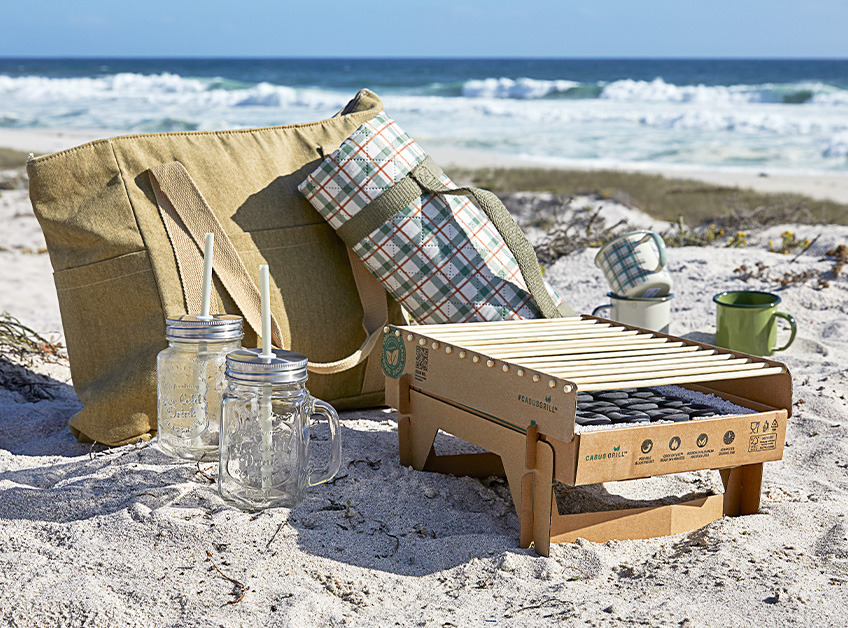 Disposable barbeque, picnic cool bag, picnic blanket, drinking glasses and cups on beach 