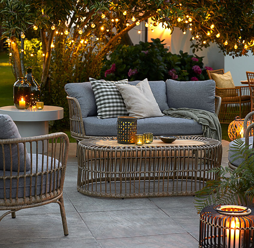 Comfortabele loungemeubelen op een terras met verlichting, batterijlampen en lantaarns met kaarsen en waxinelichtjes