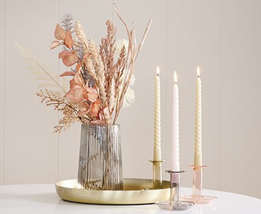 Vaas op een gouden schaal met kunstbloemen en gedraaide kaarsen in een kaarsenhouder